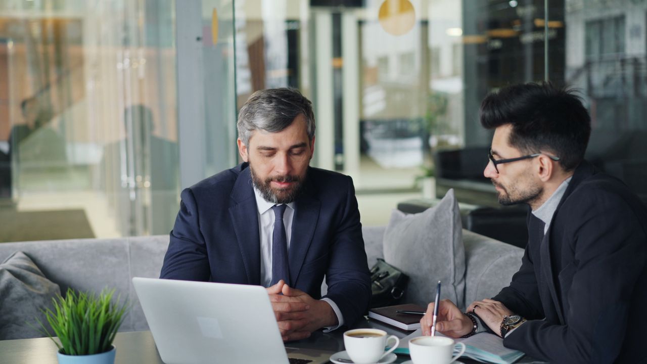 The Art of Drawing Readers In: Your attractive post title goes here Two businessmen in suits discussing work at a cafe with laptops and coffee.