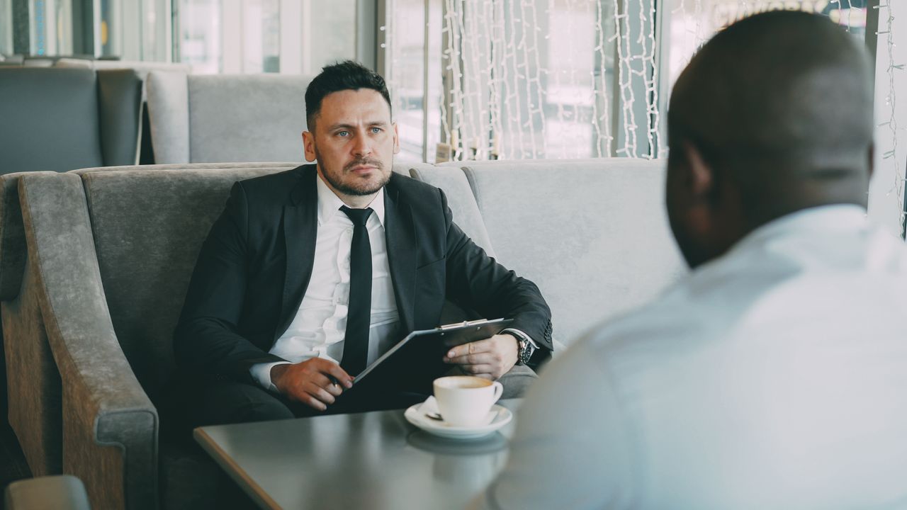 Mastering the First Impression: Your intriguing post title goes here Two businessmen having a serious conversation over coffee in a stylish cafe setting.
